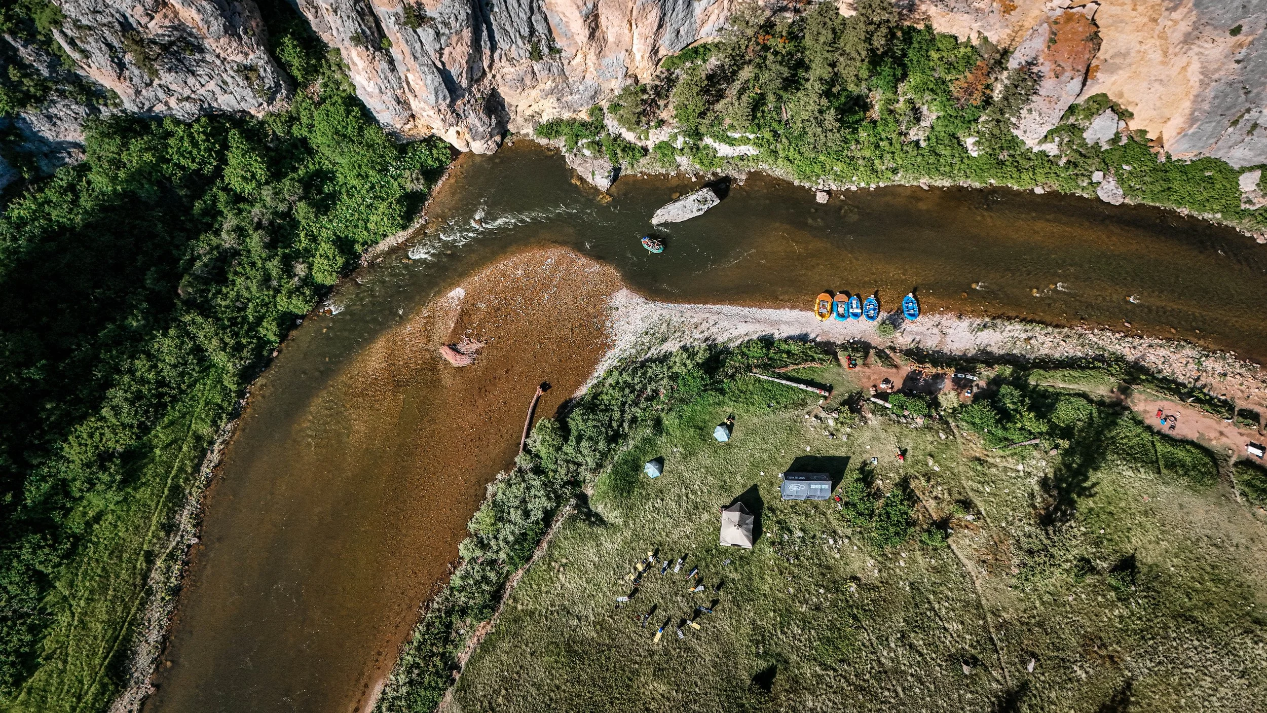 An aerial view of a river running through a green landscape, with boats parked along the shore and trees on the cliffs surrounding the river.