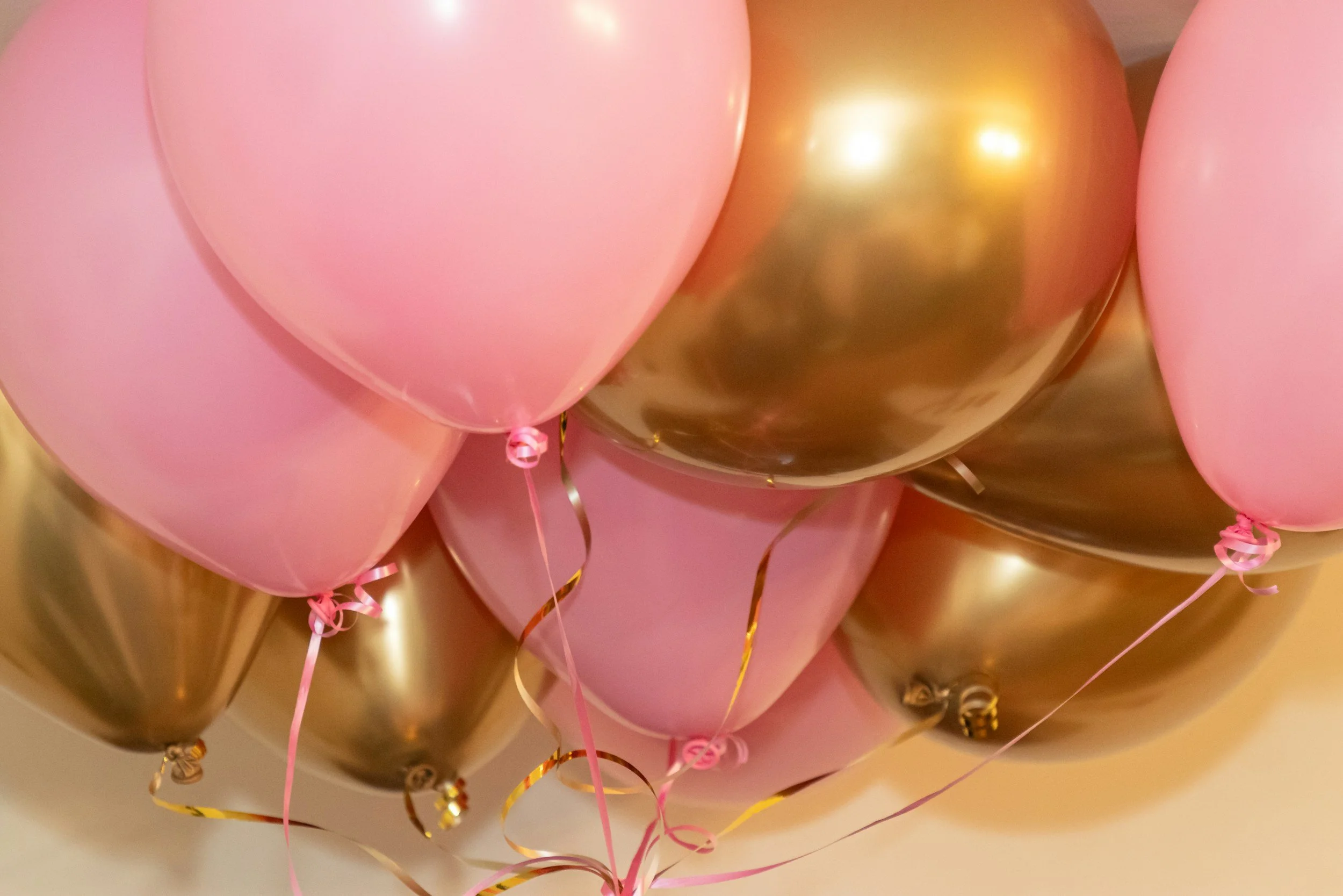 Close-up of pink and gold metallic balloons, some with curling ribbons attached, clustered together.