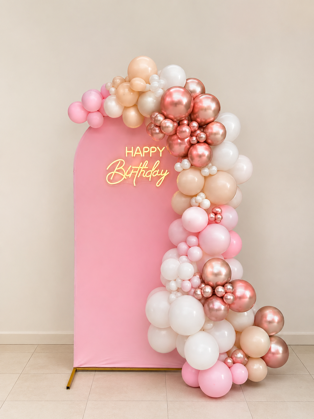 Pink backdrop with a yellow neon sign that reads 'HAPPY Birthday', decorated with a cascade of pastel and metallic balloons in shades of white, pink, cream, and rose gold.