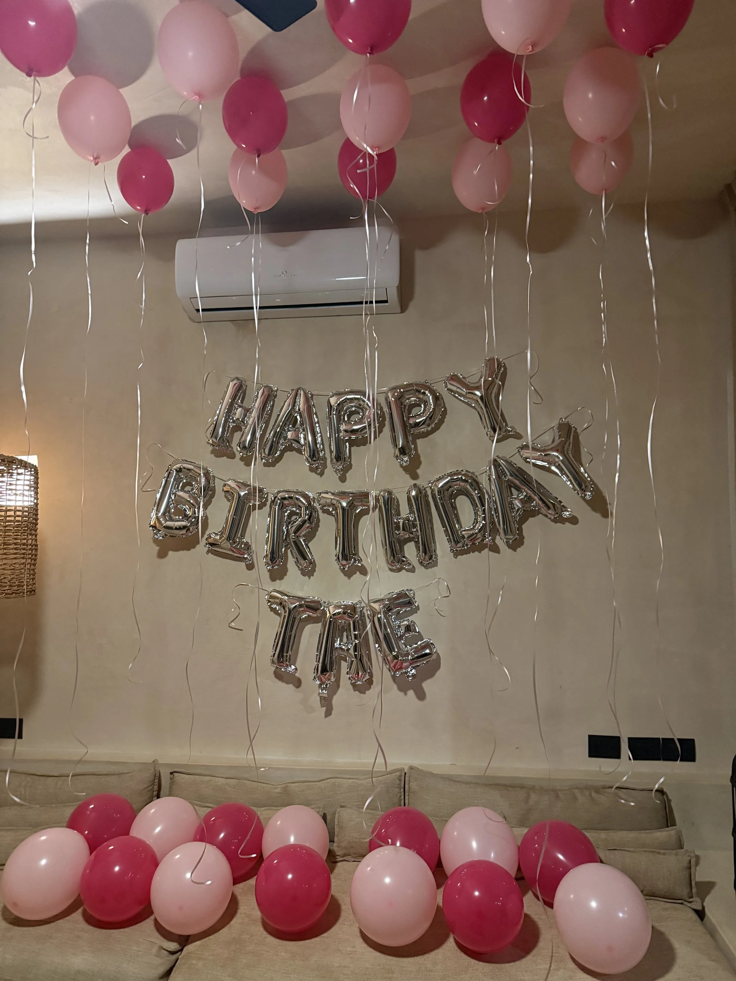 Pink and red balloons hanging from the ceiling and on the couch, with a silver 'Happy Birthday Girl' balloon banner on the wall.