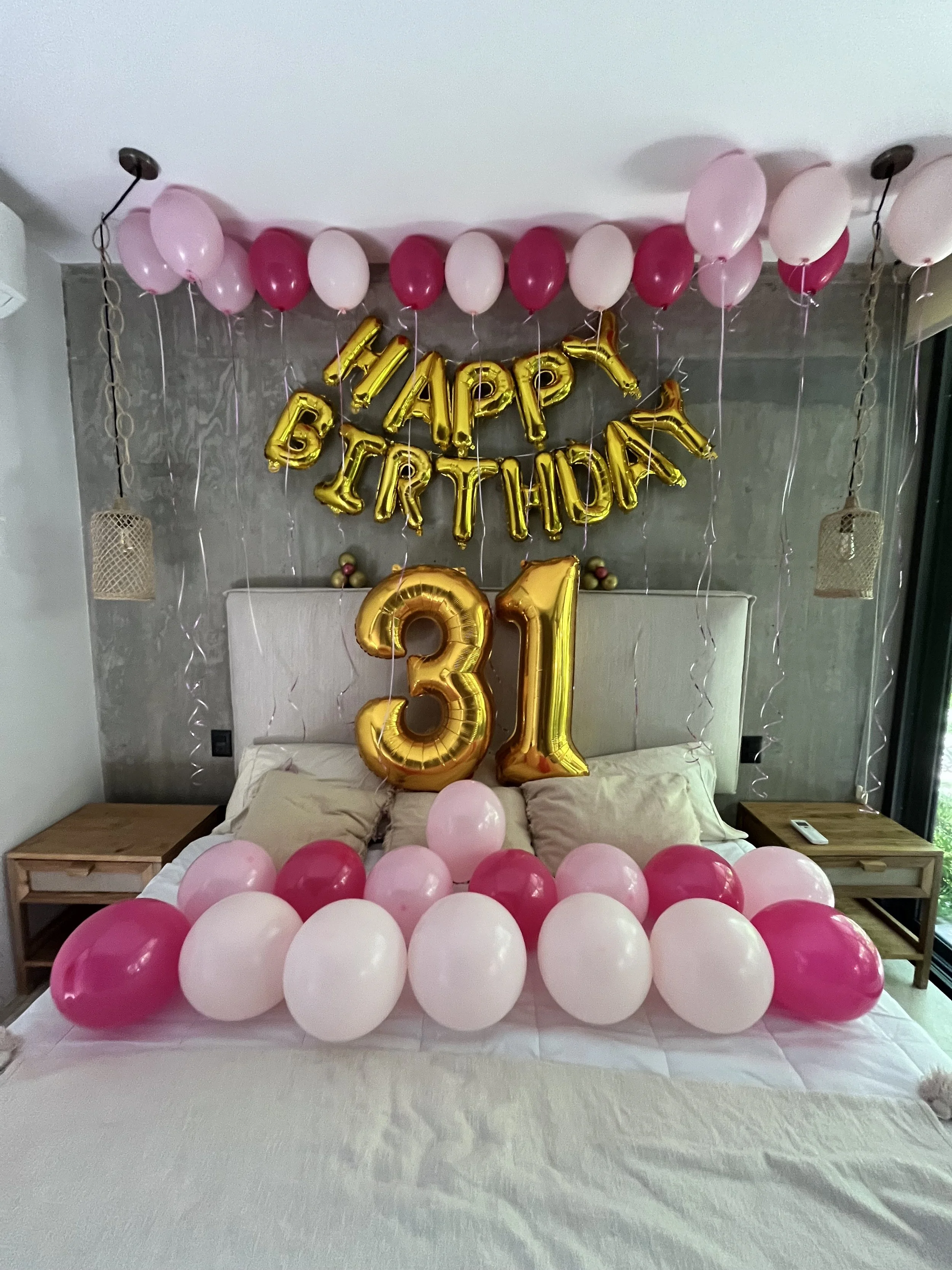Birthday decorations on a bed with pink and white balloons, golden number 31 balloons, and a 'Happy Birthday' banner.