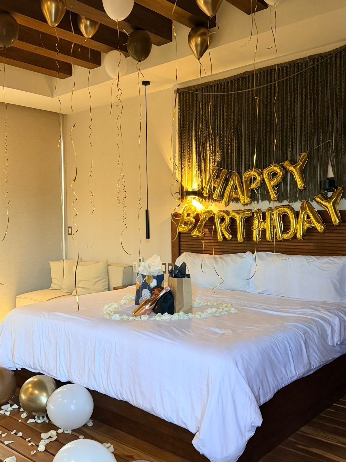 Decorated bedroom with 'Happy Birthday' balloons, balloons on the floor, and gifts on the bed.