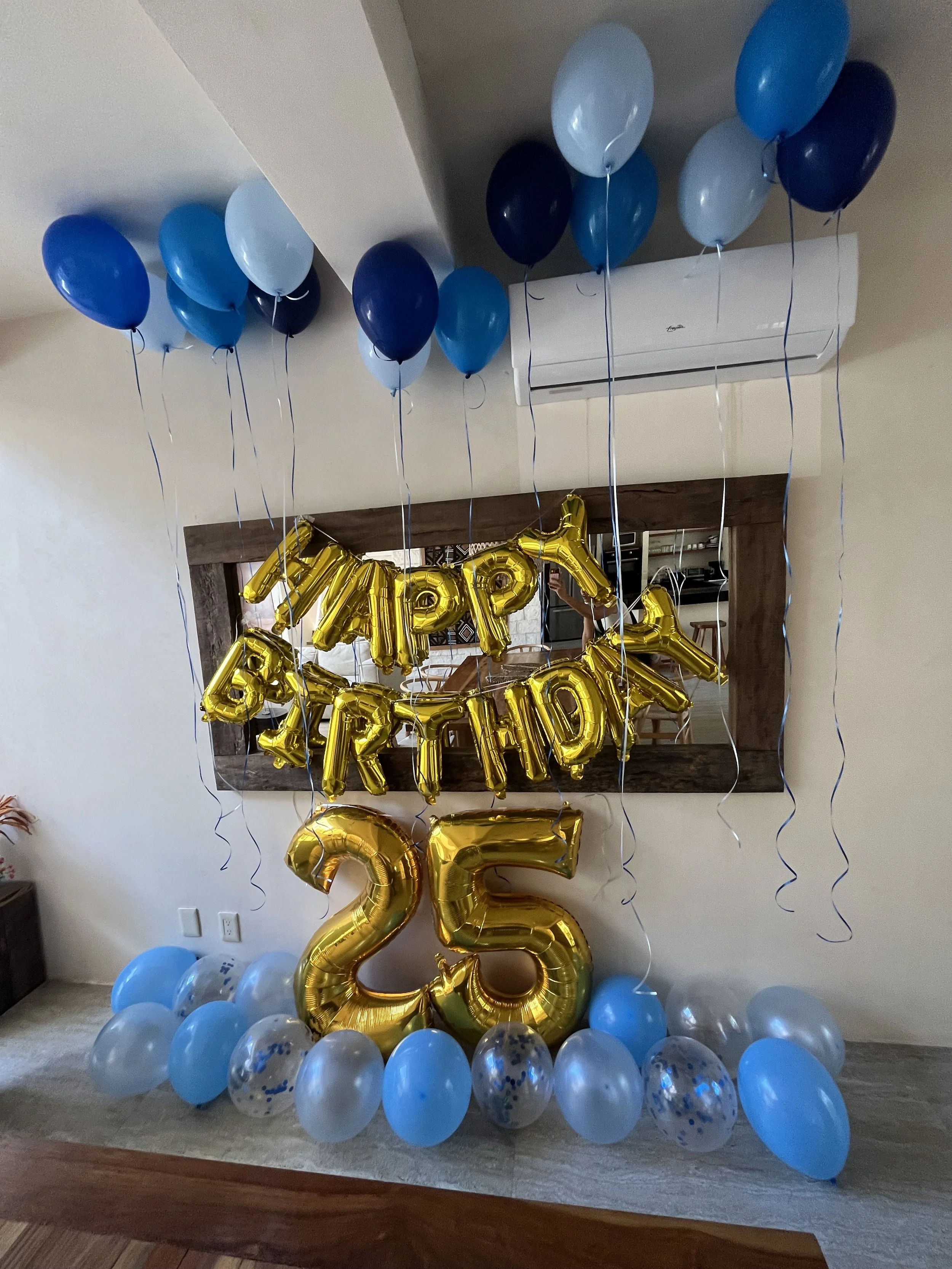 Decorations for a 25th birthday party featuring blue, white, and navy balloons, a gold 'HAPPY BIRTHDAY' banner, and a large gold number '25' balloon.