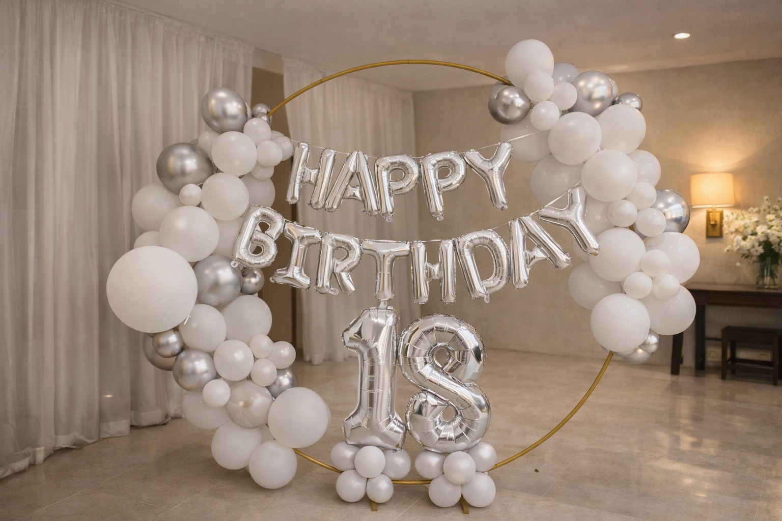 Balloon decoration with silver and white balloons forming a circular frame, with silver letter balloons spelling 'HAPPY BIRTHDAY' and a large silver number 18, used for birthday celebration.