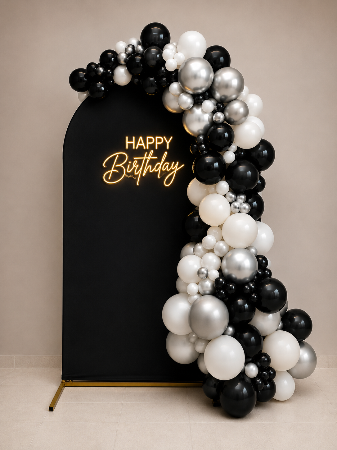 Black photo backdrop with a "Happy Birthday" neon sign and a balloon arrangement of black, white, pearl, and silver balloons on the right side.
