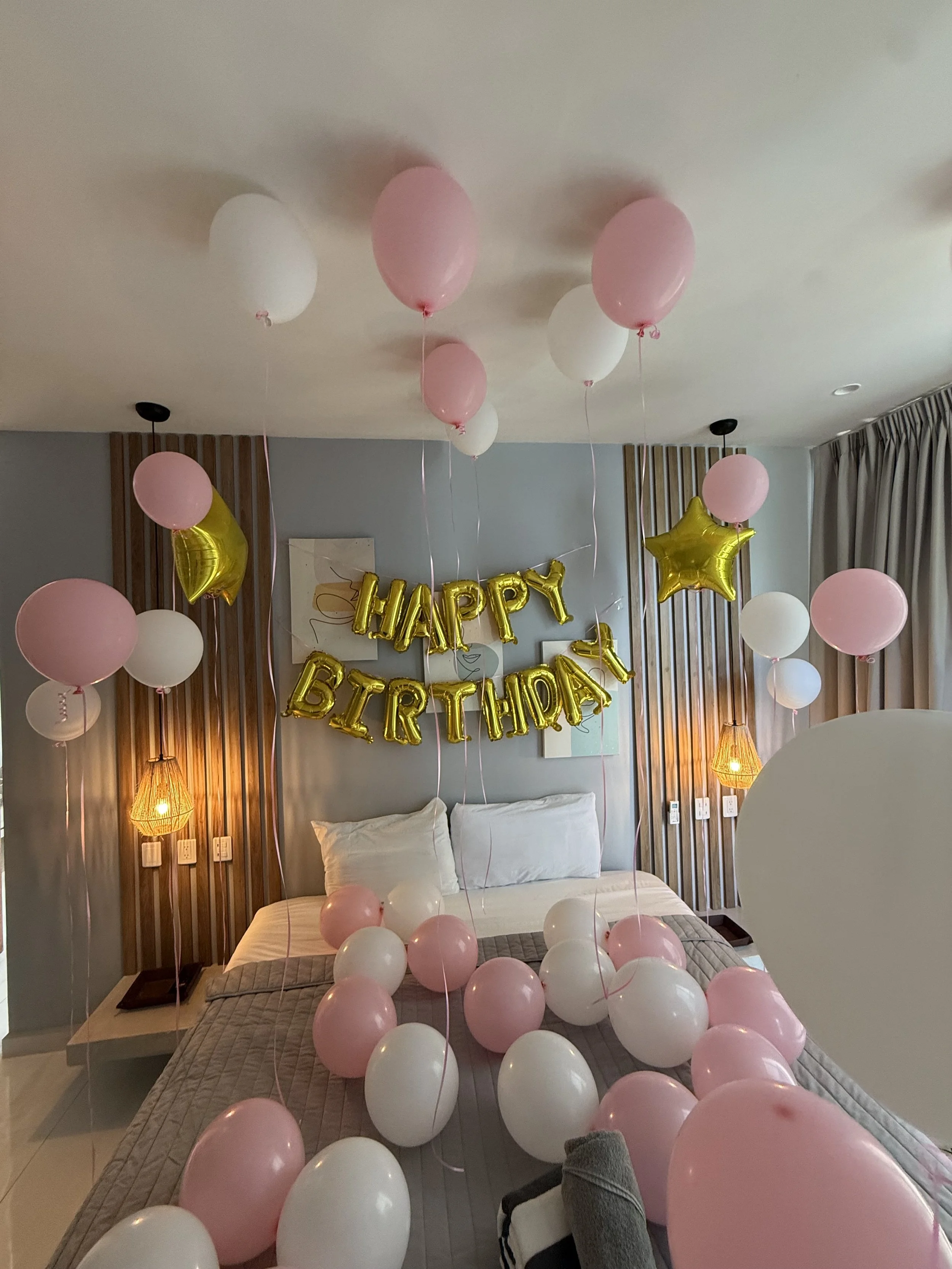 Decorated bedroom with pink and white balloons, golden star-shaped balloons, and a 'Happy Birthday' banner on the wall.