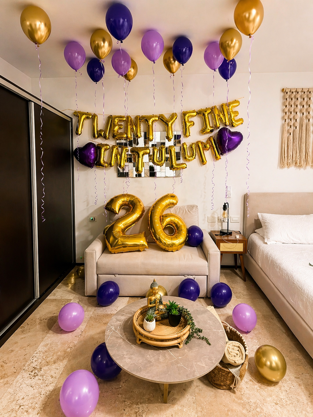 Celebration decor on a living room wall with gold and purple balloons, gold letter balloons spelling 'Twenty Fine, Contentulum,' and large gold number balloons '26' on a beige couch, surrounded by purple and pink balloons, with a Buddha statue and po