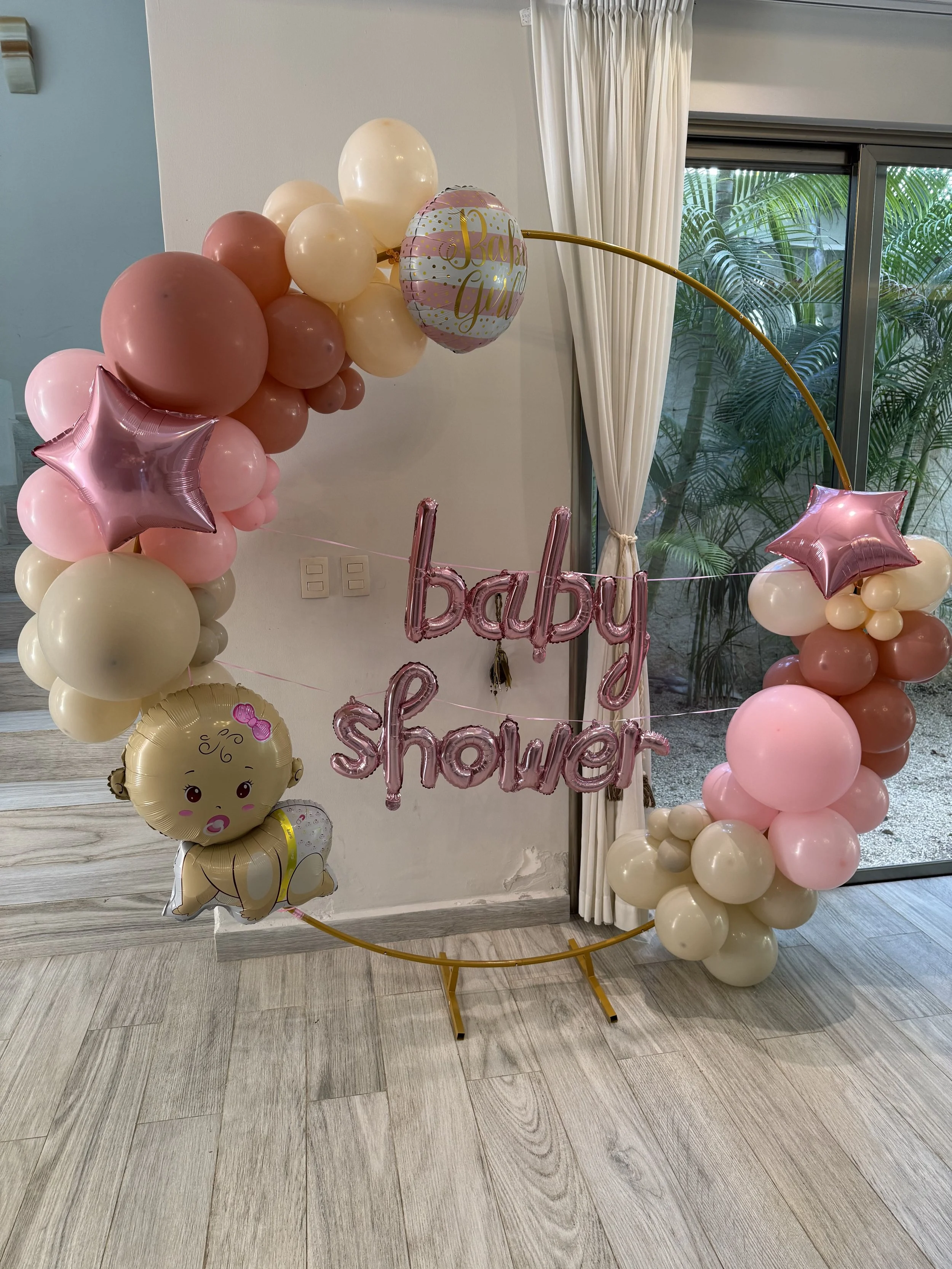 Baby shower decoration with pink and beige balloons arranged in a circular shape, a pink balloon arch, and signs reading "baby shower" with a balloon girl figure.