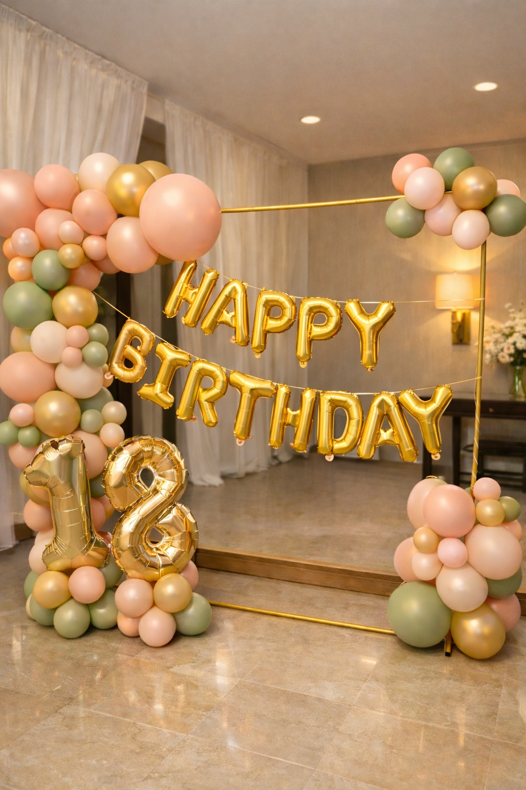 Decorations for a birthday celebration with pastel-colored balloons and gold foil balloons that spell out "HAPPY BIRTHDAY." A large gold number "12" balloon is on the floor. The background features a mirror, white curtains, and a floral arrangement.