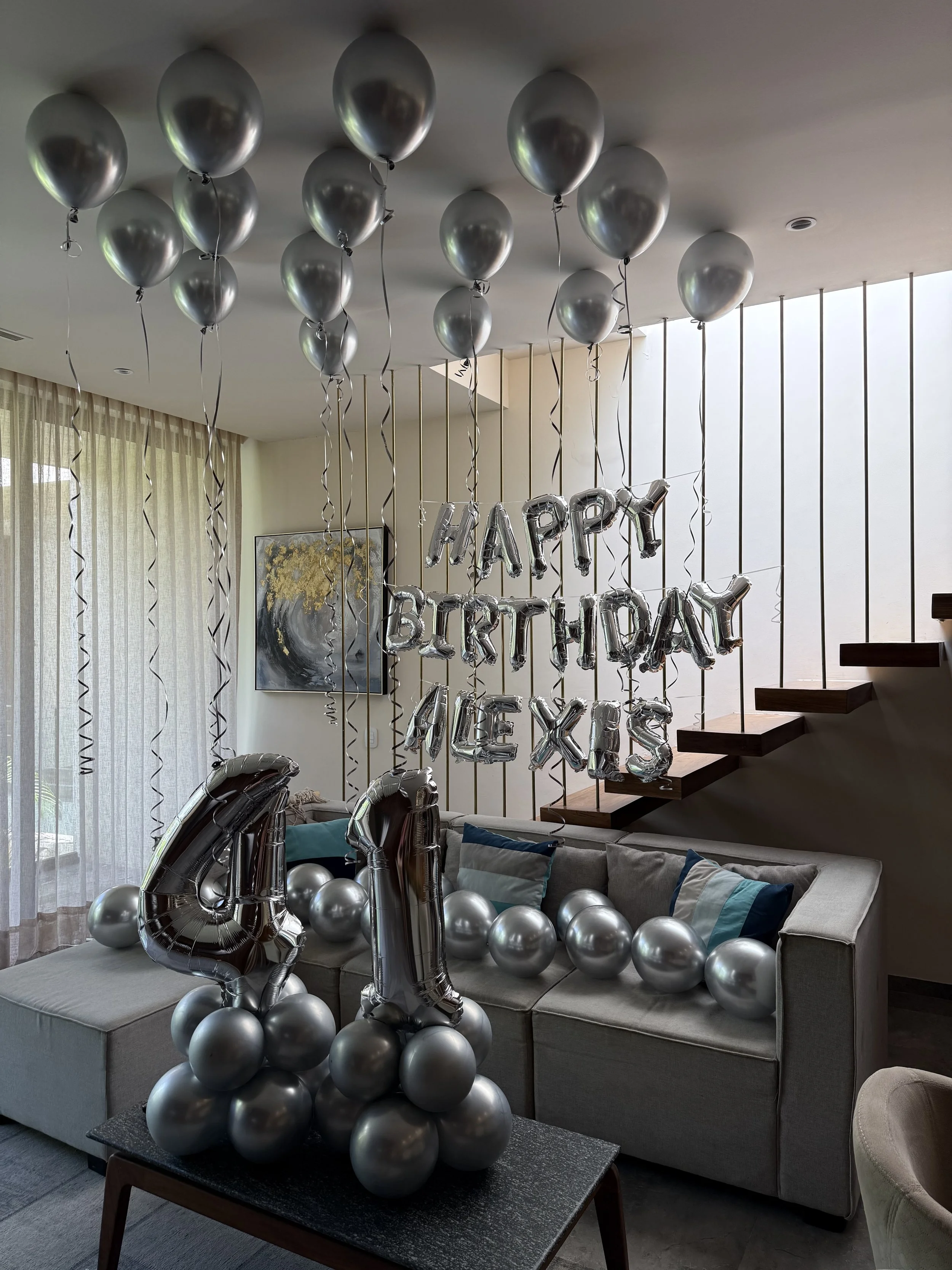 Silver balloons with metallic finish, some shaped as numbers, decorating a living room for a birthday celebration with 