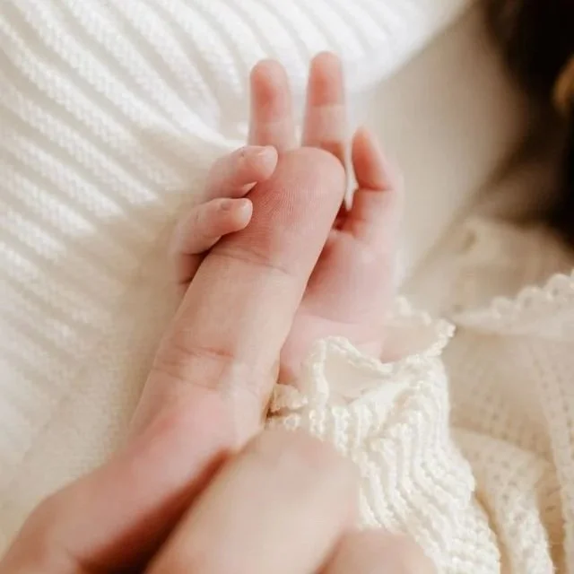 La mano di un neonato stringe il dito di un adulto.