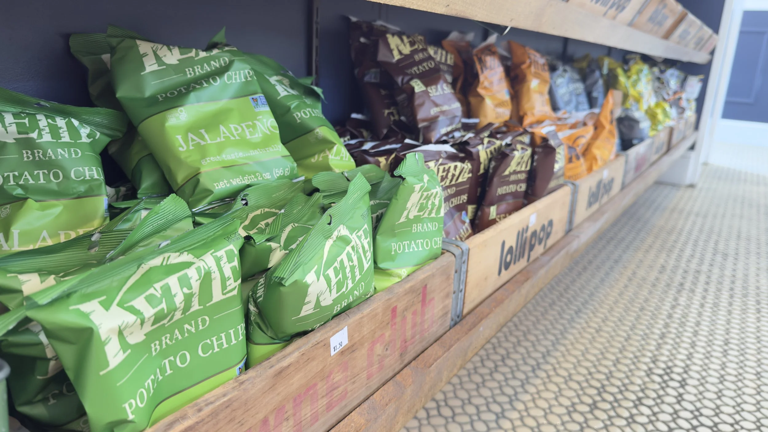 Various bags of potato chips on display on wooden shelves in a store aisle.