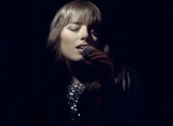 Una donna che canta con un microfono in mano, scena di un'esibizione musicale in bianco e nero.