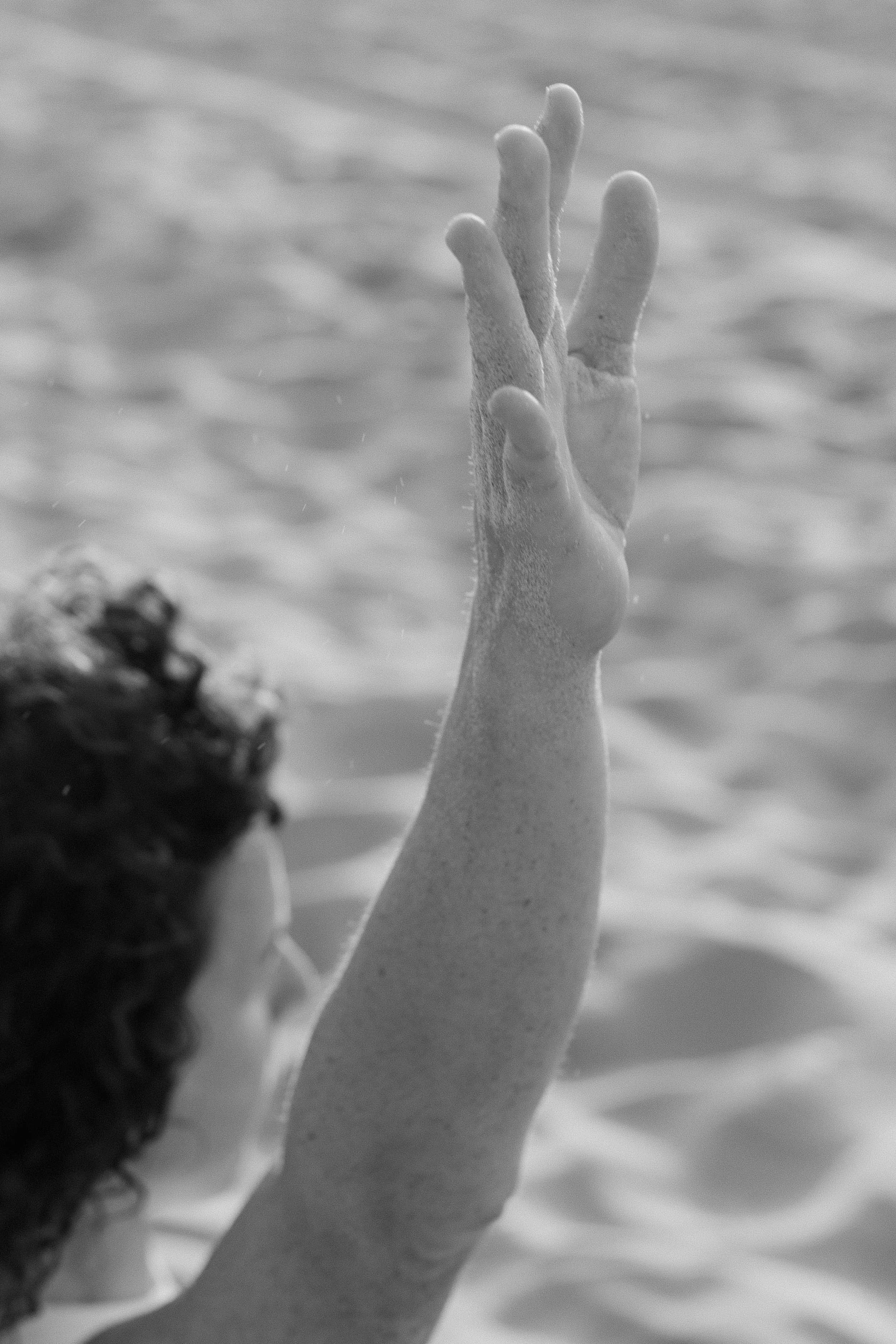 Black and white photo of a hand emerging from the water, with fingers reaching upward.