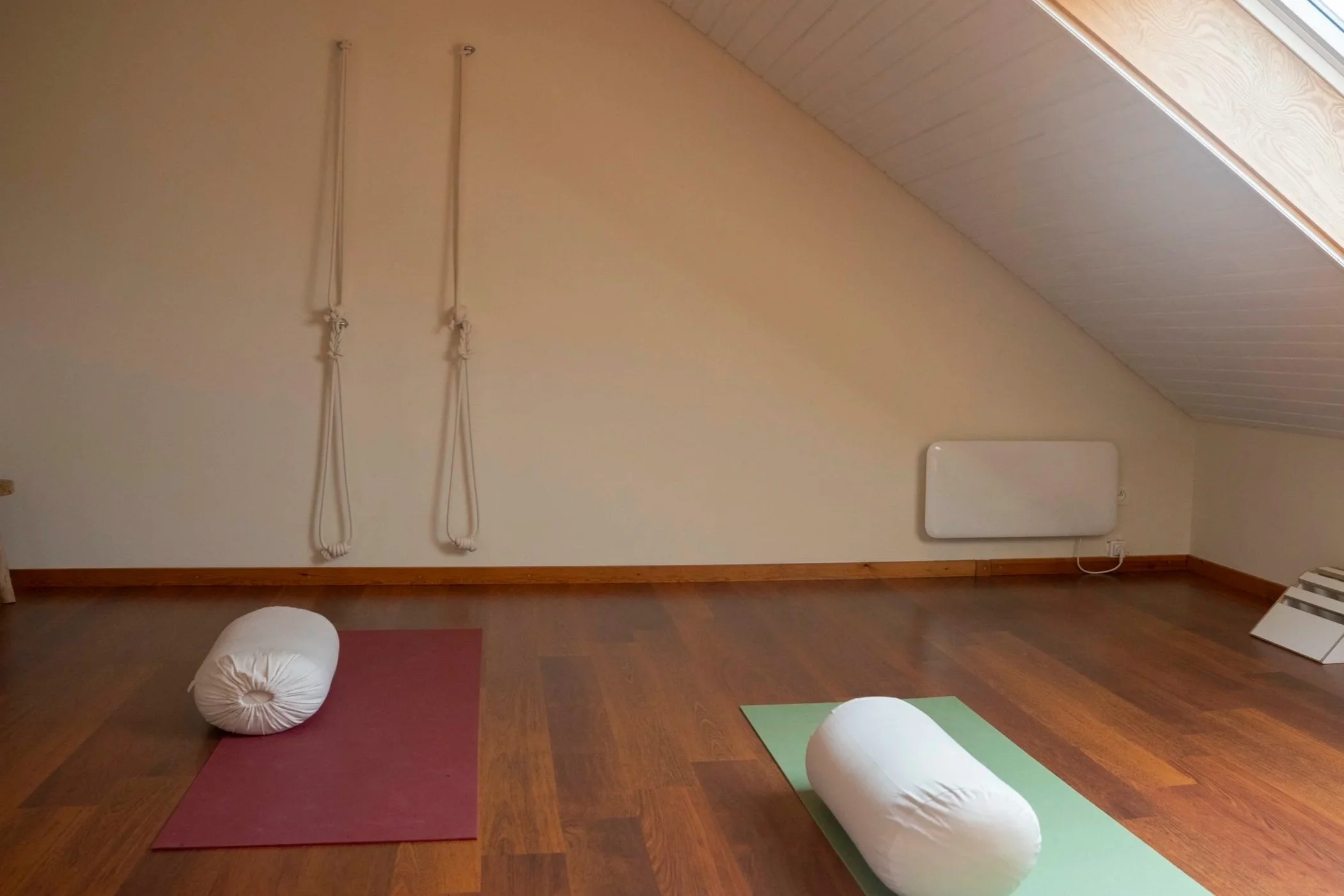 A yoga or meditation room with mats, bolsters, and a hammock or swing hanging from the ceiling against an angled wall with a heater nearby.