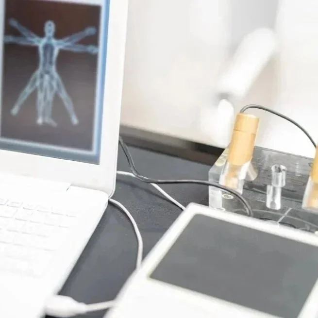 A computer displaying a human body scan, with a black and gray object in front of it and wires connected to medical equipment.