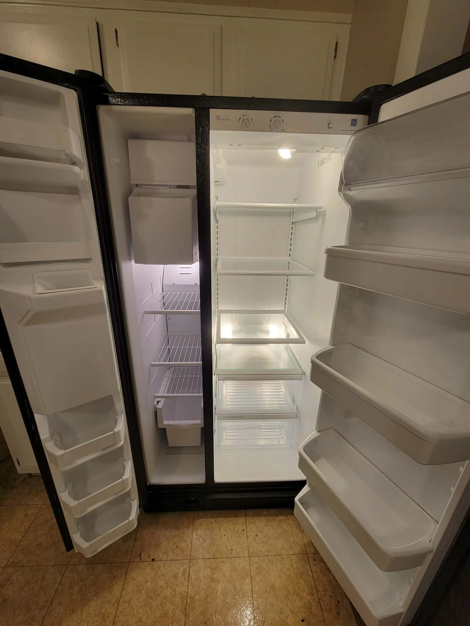 Inside of an empty side-by-side refrigerator with doors open, showing shelves and compartments.