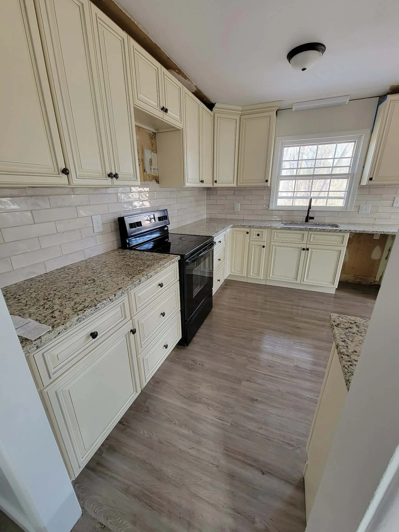 Kitchen with beige cabinets, granite countertops, black stove, white subway tile backsplash, and a window above the sink.