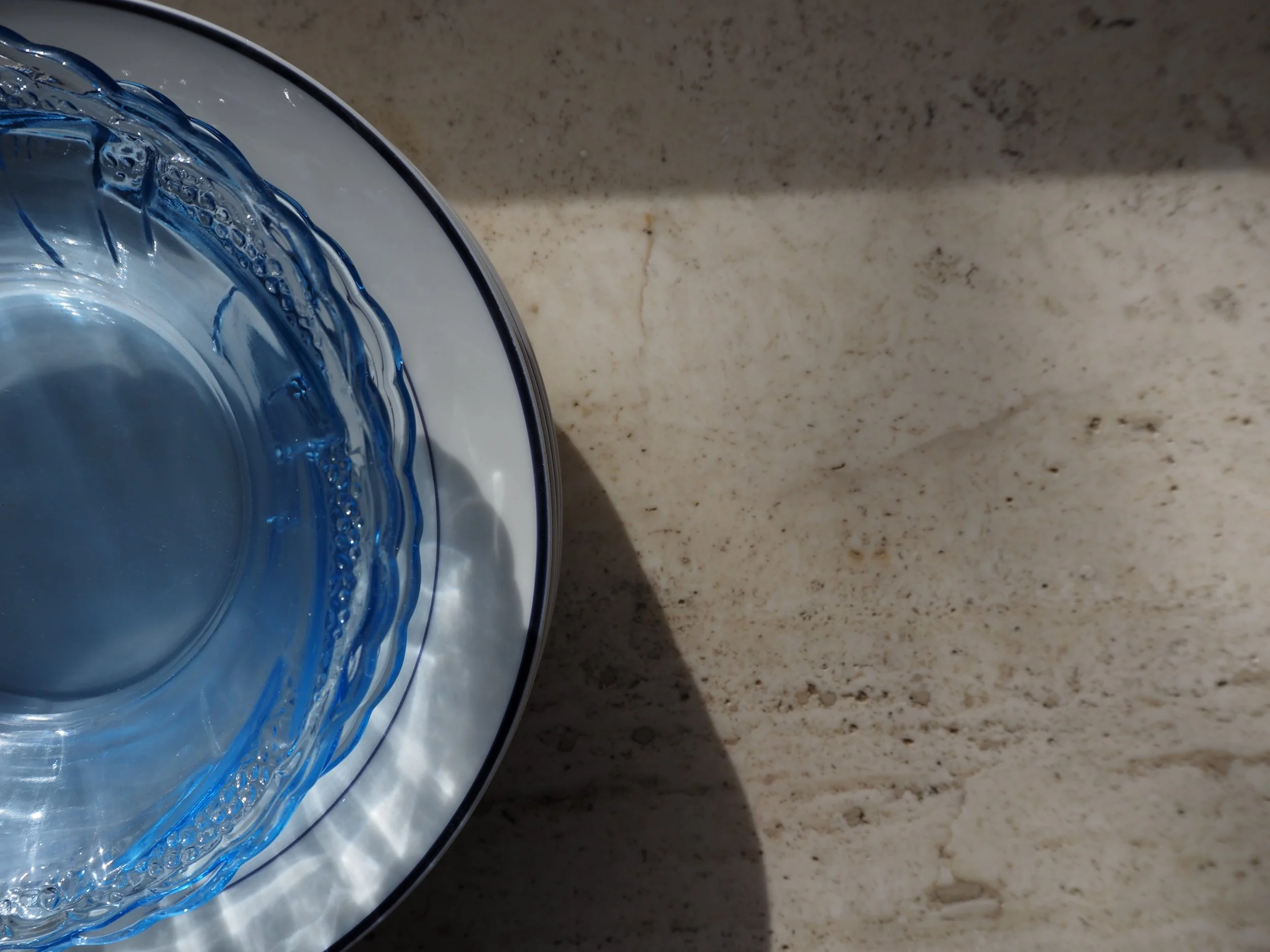 A top-down view of a glass bowl filled with water sitting on a white dish on a beige marble countertop.