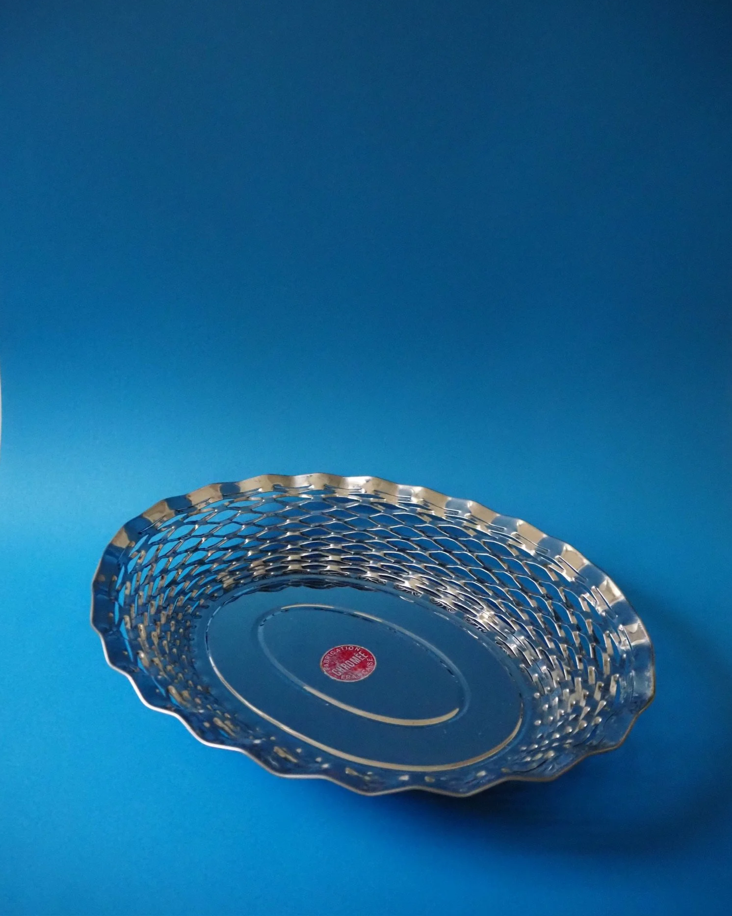 A clear glass decorative bowl with scalloped edges, placed on a blue surface with a blue background.