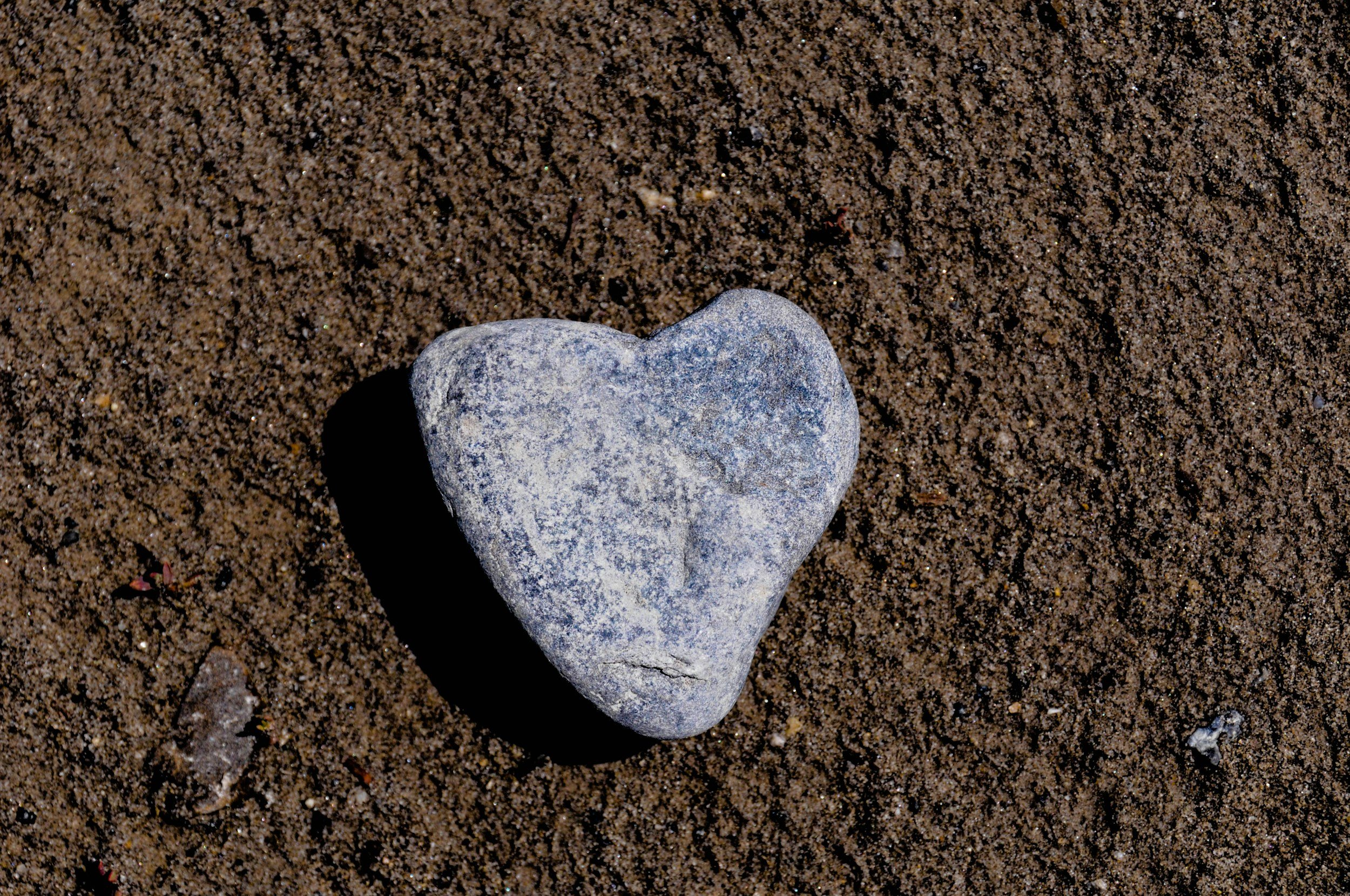 A heart-shaped gray stone on sandy ground.