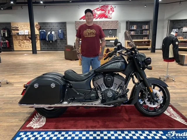 A young man standing behind a black motorcycle inside a retail store.