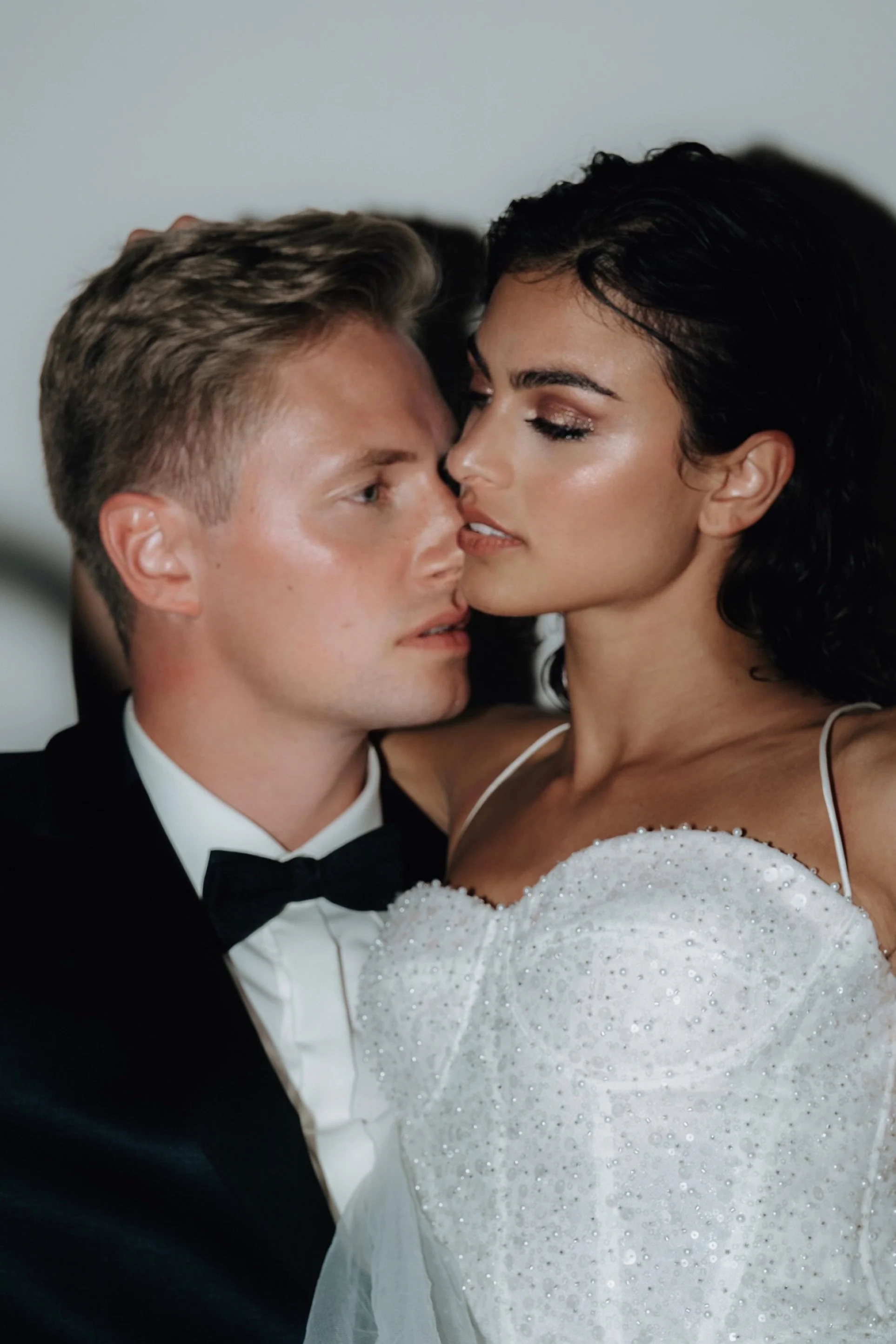 Ein Brautpaar bei einer Hochzeit, der Mann trägt einen schwarzen Anzug mit Fliege und das Mädchen ein weißes Hochzeitskleid mit Pailletten.