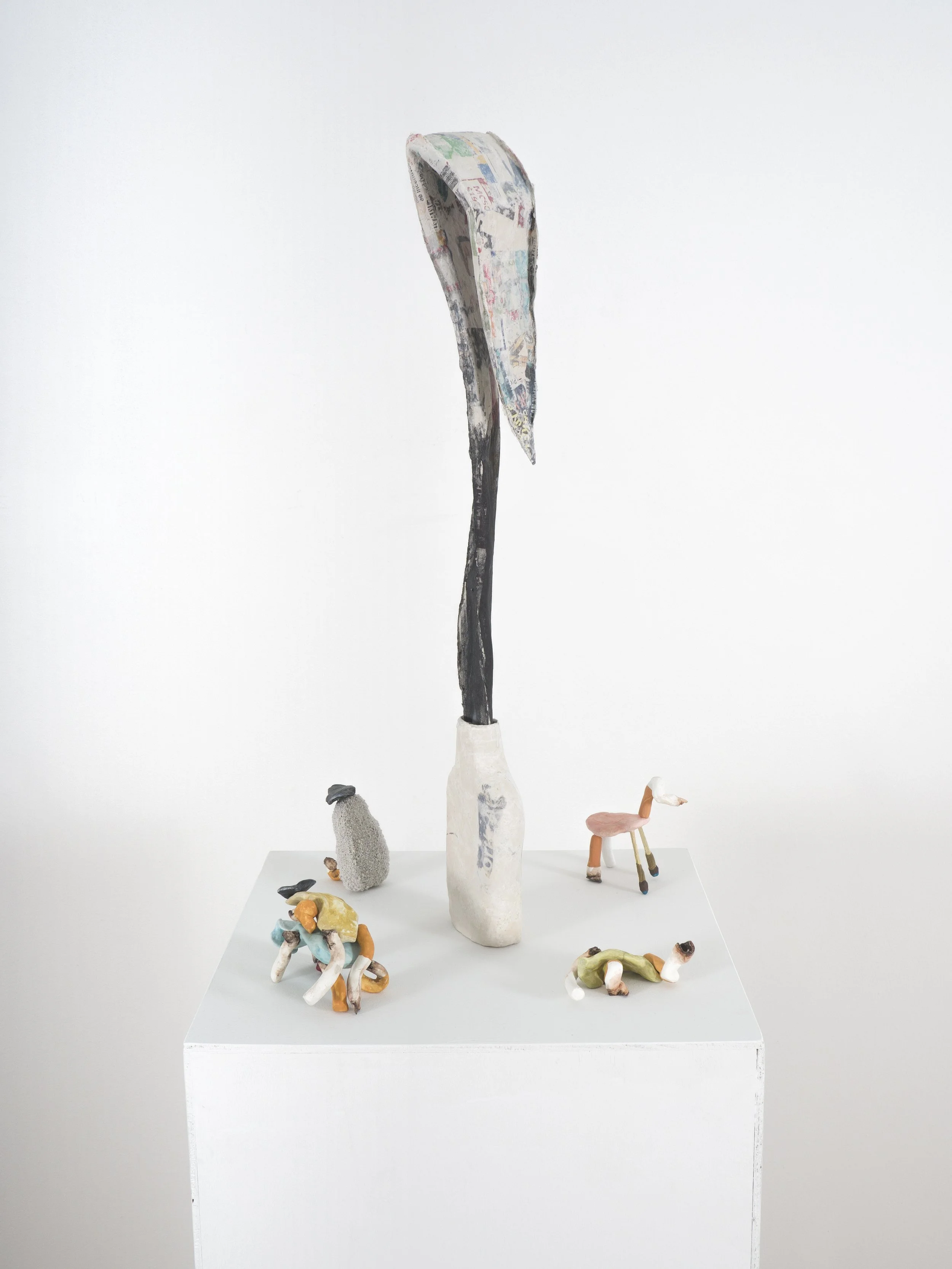 Sculpture with a tall, curved object resembling an axe or sickle behind four small ceramic animal figures on a white pedestal.
