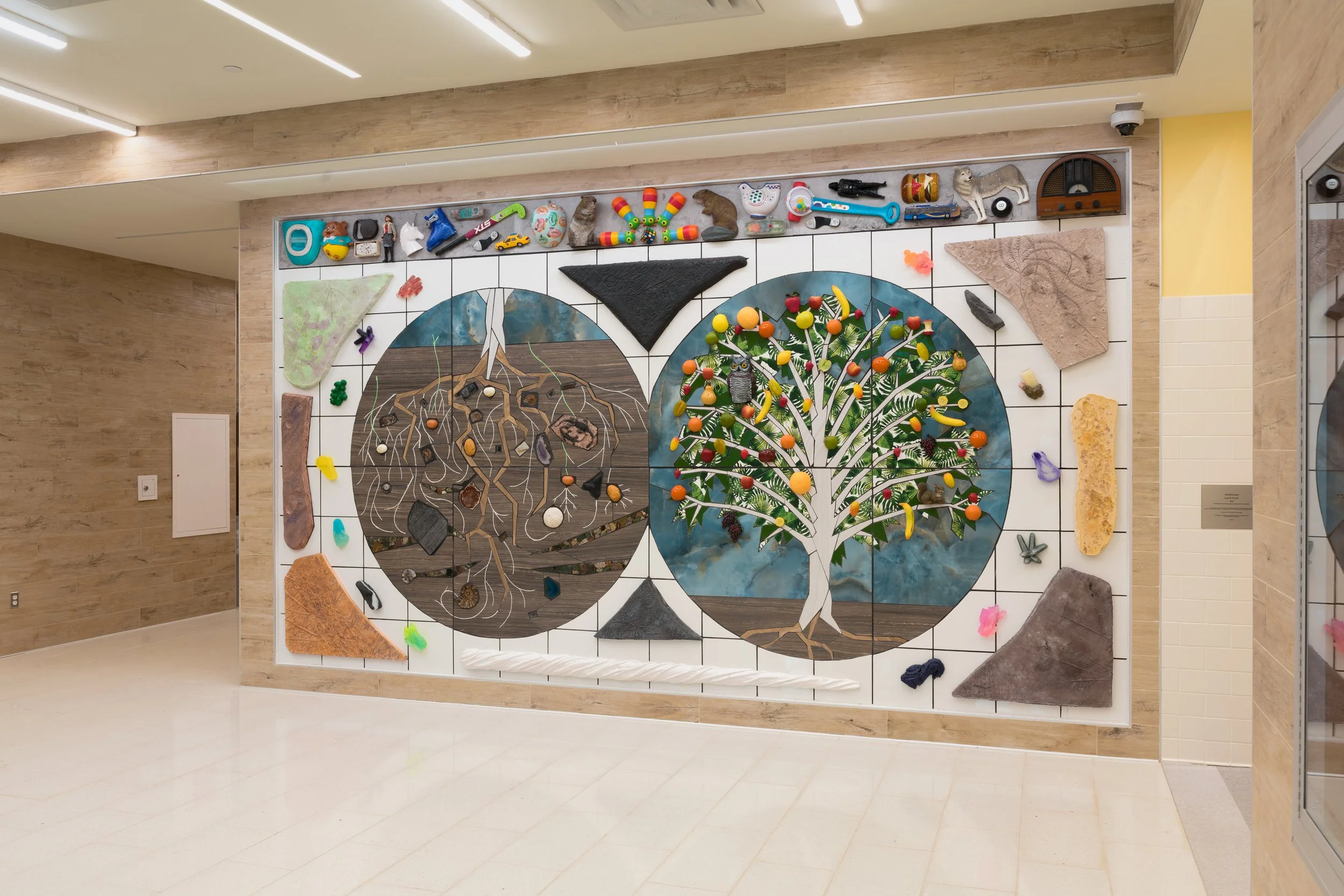 Art installation depicting the cycle of a tree, with a desert scene on the left and a lush, fruit-bearing tree on the right, made from various materials and objects.