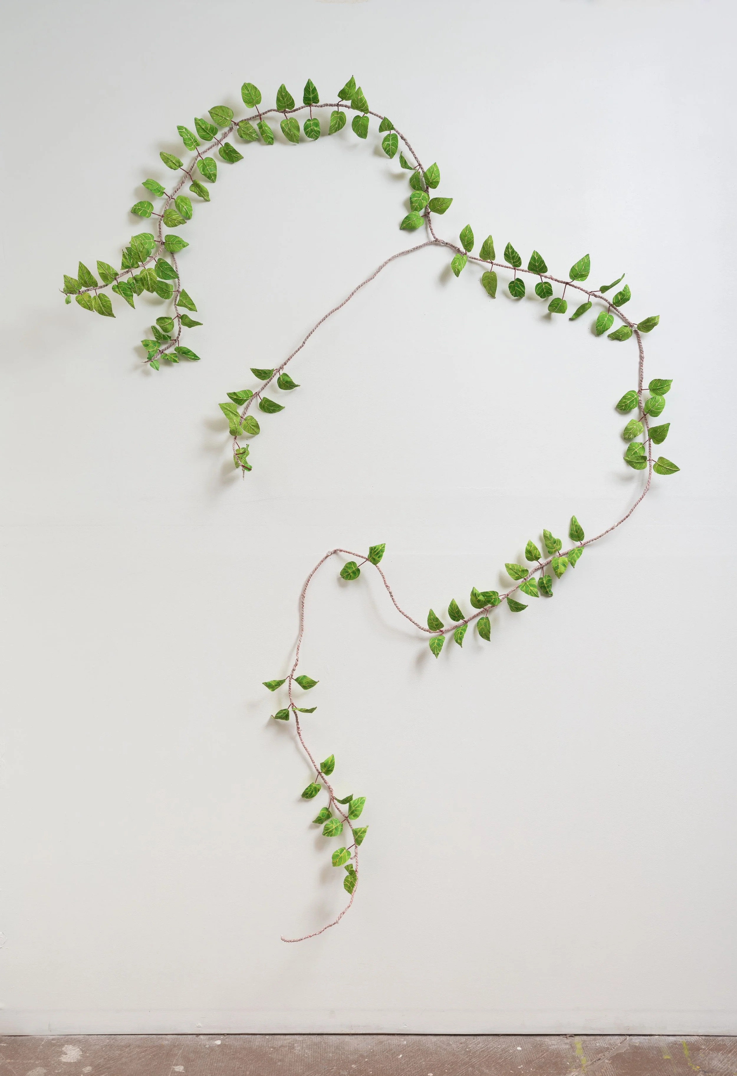 A wall decoration made of green ivy leaves arranged in a shape resembling a question mark on a plain white wall.
