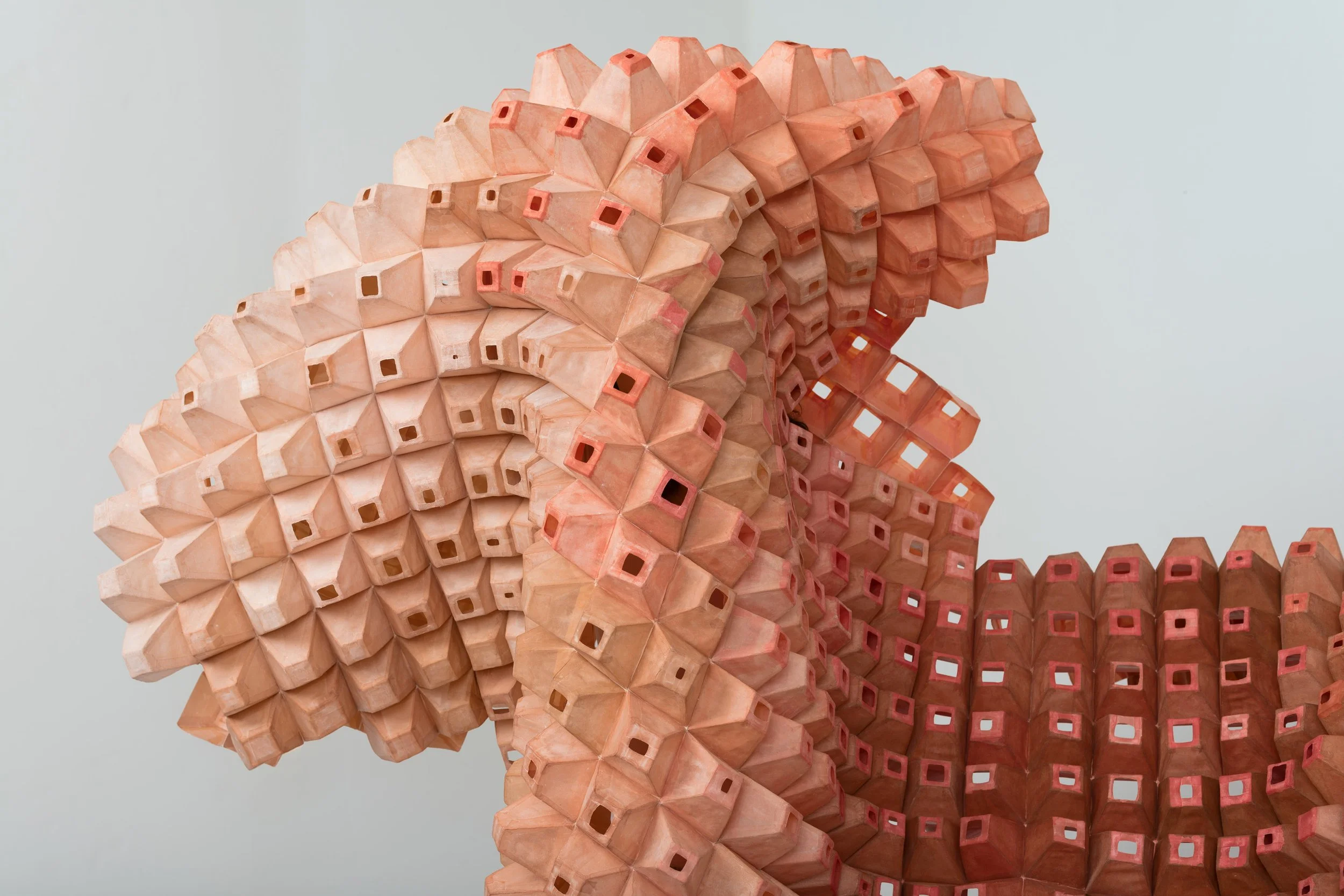 A close-up view of a sculptural installation made from numerous pinkish-orange colored wooden pencil tips arranged in a flowing, wave-like pattern.