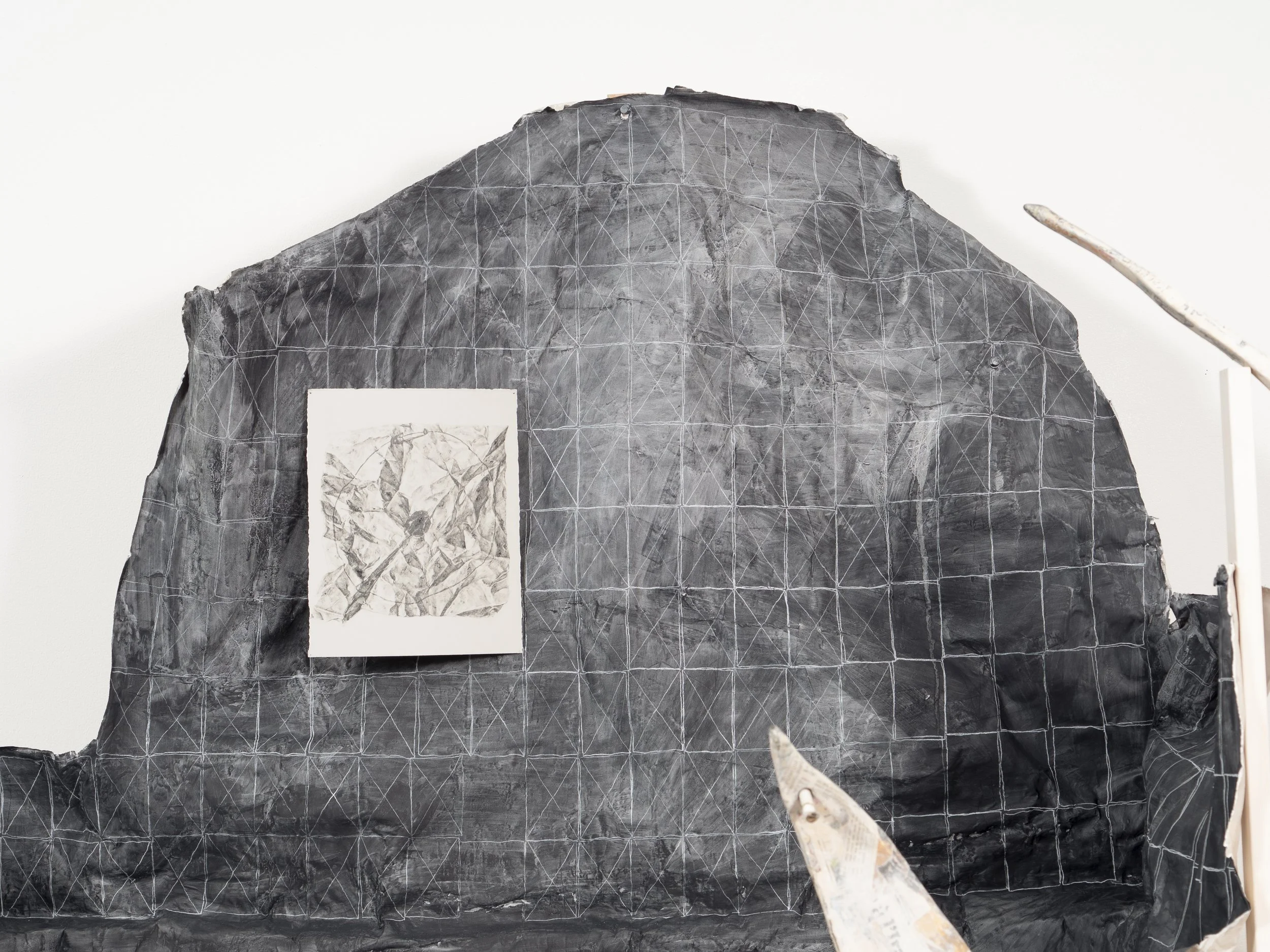A large black rock with a grid pattern drawn on it, and a smaller piece of paper with a sketch or drawing attached to it, held in place on the rock.