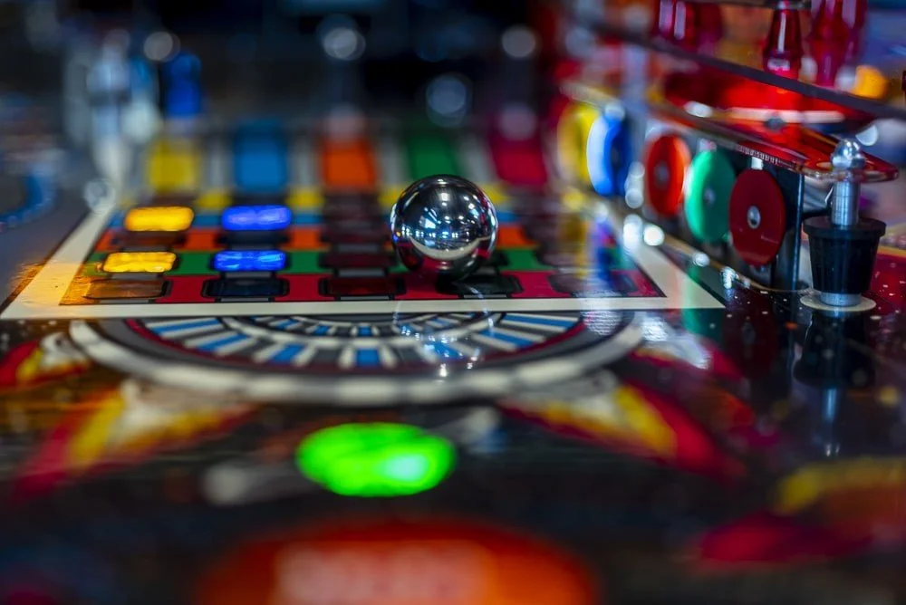 Close-up of a pinball machine with a shiny silver ball in the center, colorful bumpers, and flashing lights.