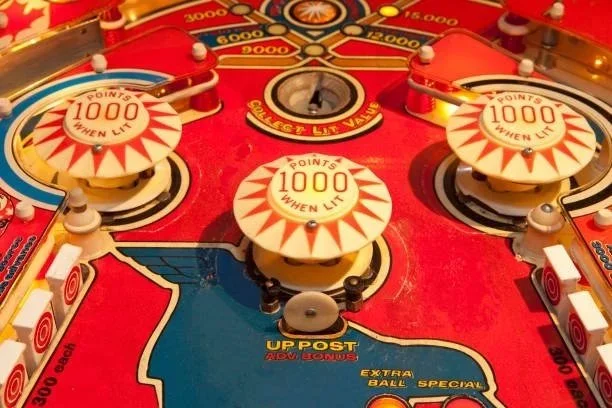 Close-up of a vintage pinball machine playfield with bumpers labeled '1000 Points When Lit,' flippers, and various targets and scoring zones.