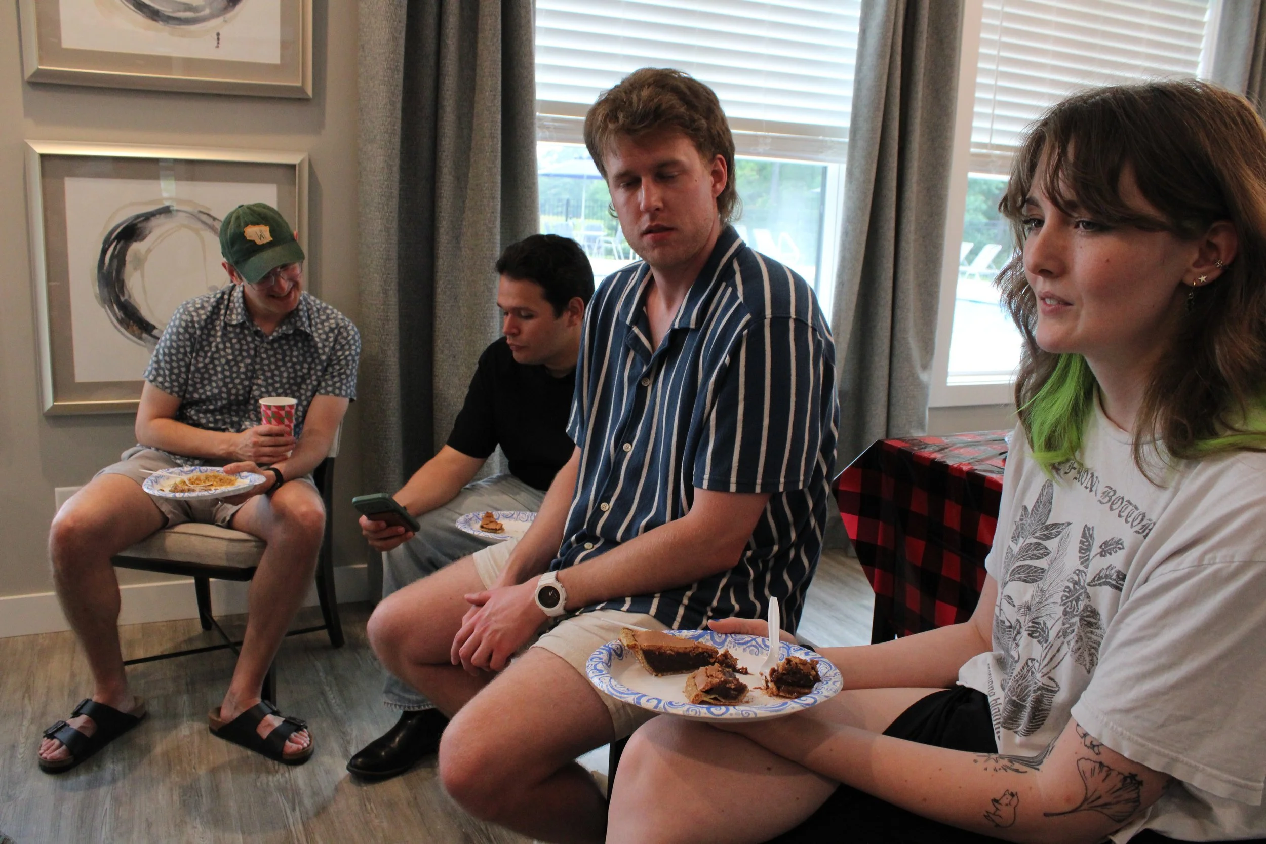 A group of tabletop gaming community members chatting and eating together on couches at a Triangle QuestHouse gathering