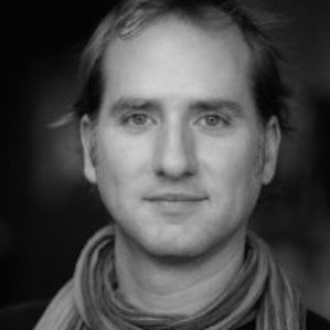 Black and white portrait of a man with short hair and a slight smile, wearing a scarf.