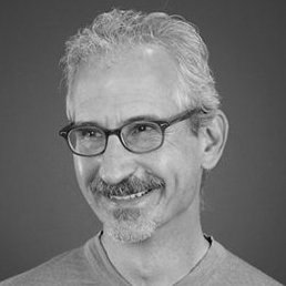 Black and white headshot of a smiling man with glasses and gray hair.