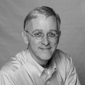 Black and white portrait of a middle-aged man with glasses, short hair, and a slight smile, wearing a collared shirt.