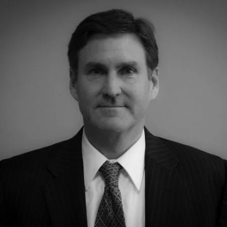 A black and white professional portrait of a man in a suit and tie, facing forward against a plain background.