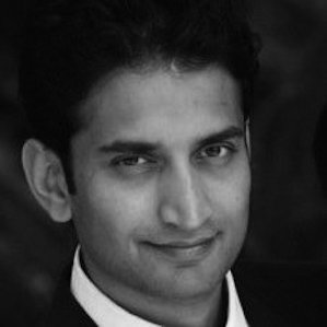 Black and white portrait of a young man with dark hair, smiling slightly, wearing a suit and tie.