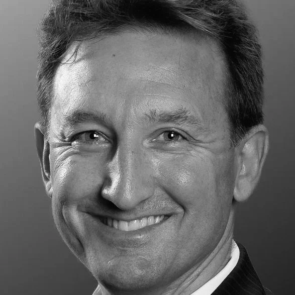 Black and white close-up portrait of a smiling man with short hair and light-colored eyes.