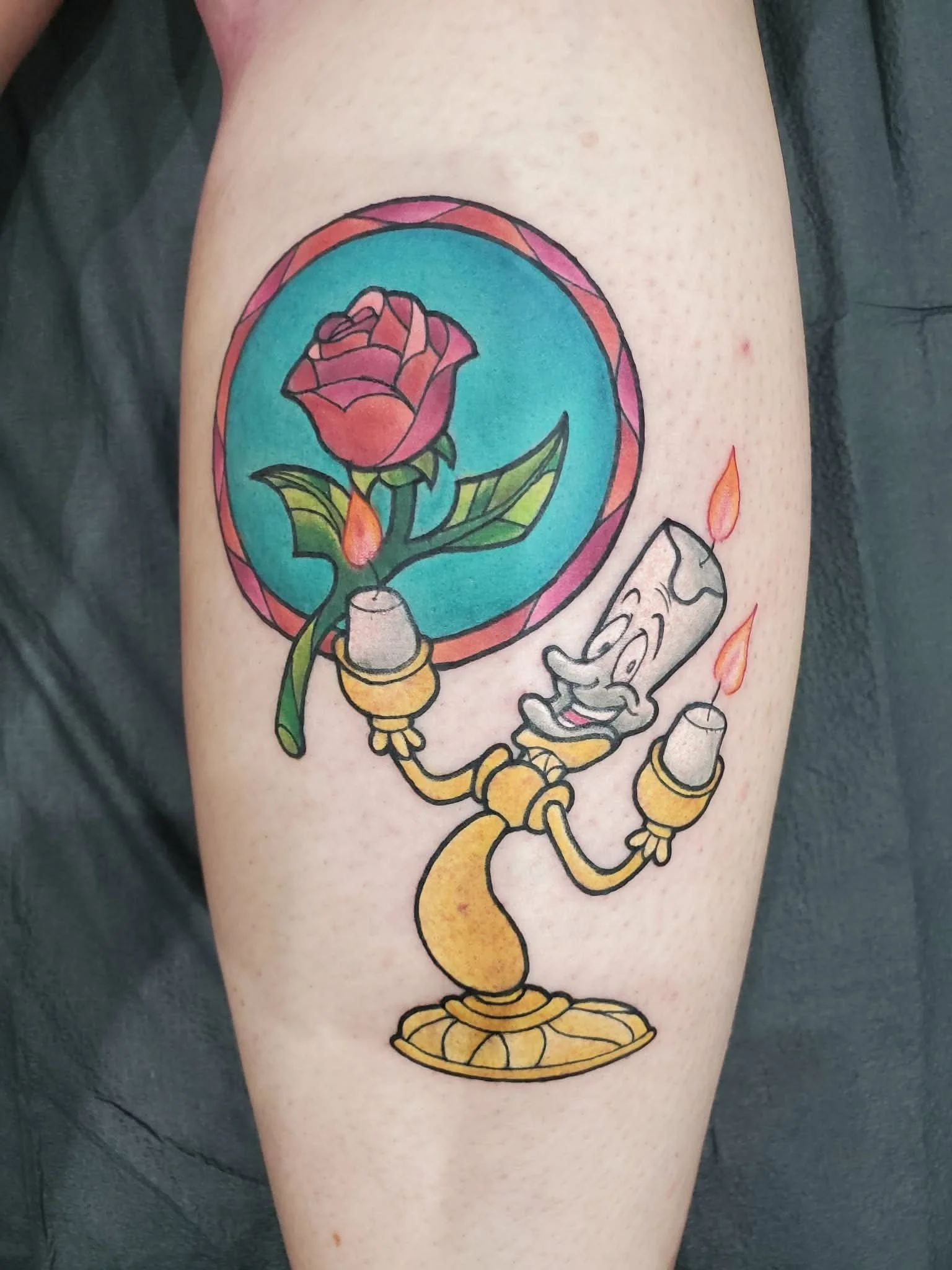 Colorful tattoo of Lumière the candelabrum from Beauty and the Beast, holding a Disney rose in a stained glass style background.