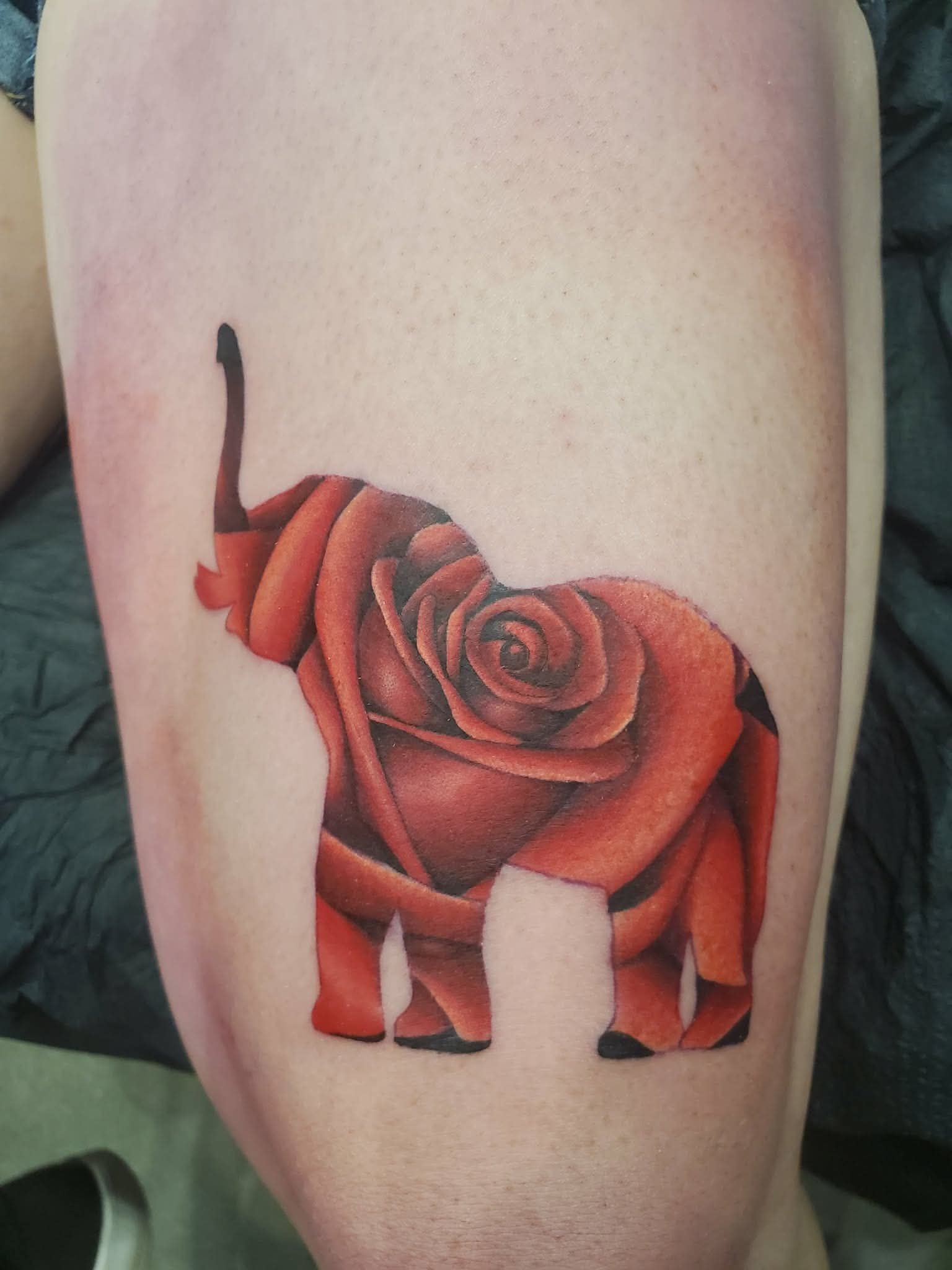 Tattoo of a red rose with an elephant shape in the petals on someone's leg.