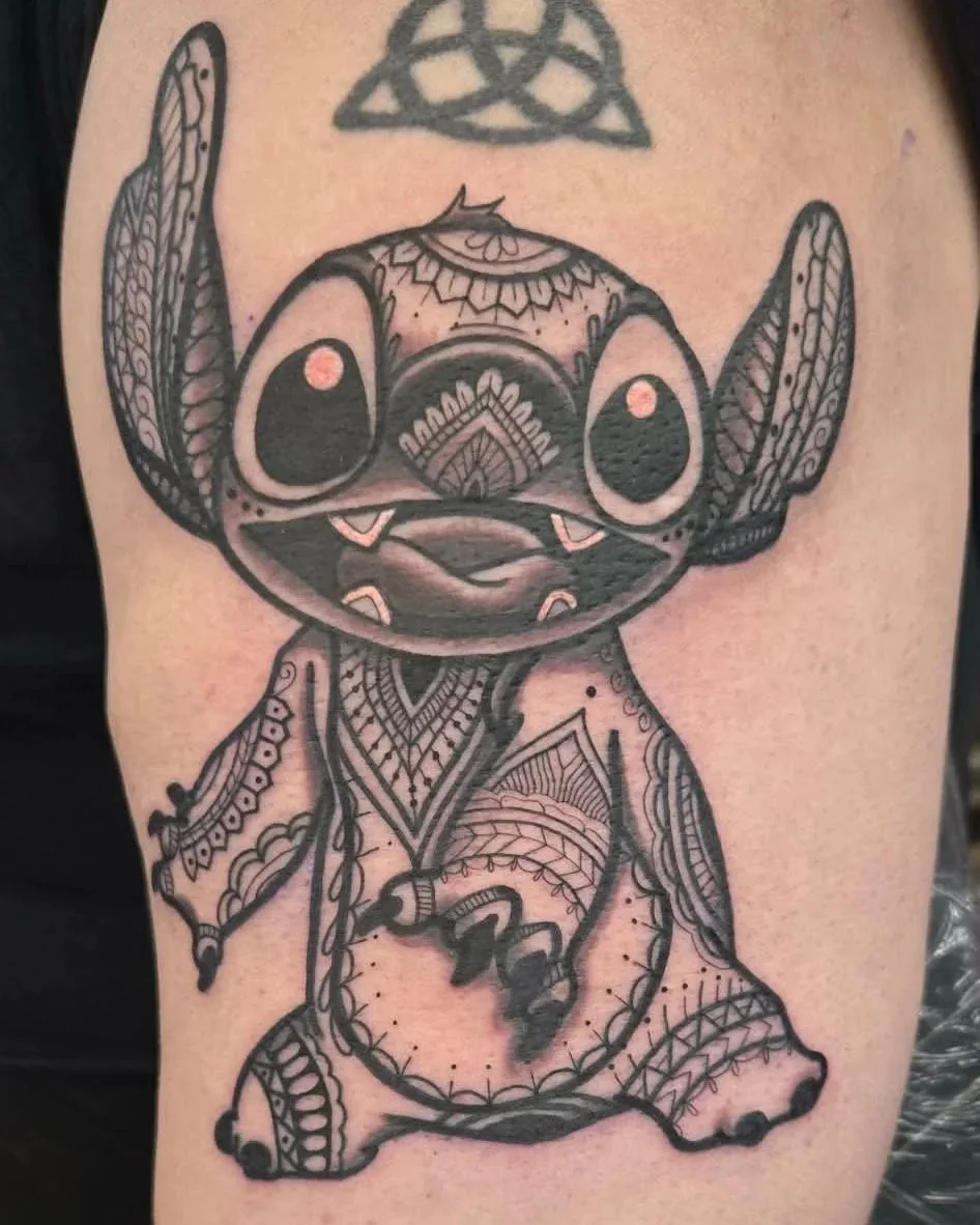 Tattoo of a stylized Disney’s character Stitch with intricate tribal patterns, in black ink on skin.