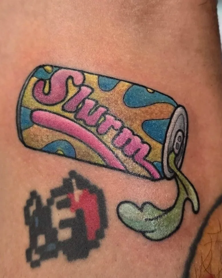 Colorful tattoo of a soda can with pink, blue, and yellow splashes, with green liquid dripping from the tab.