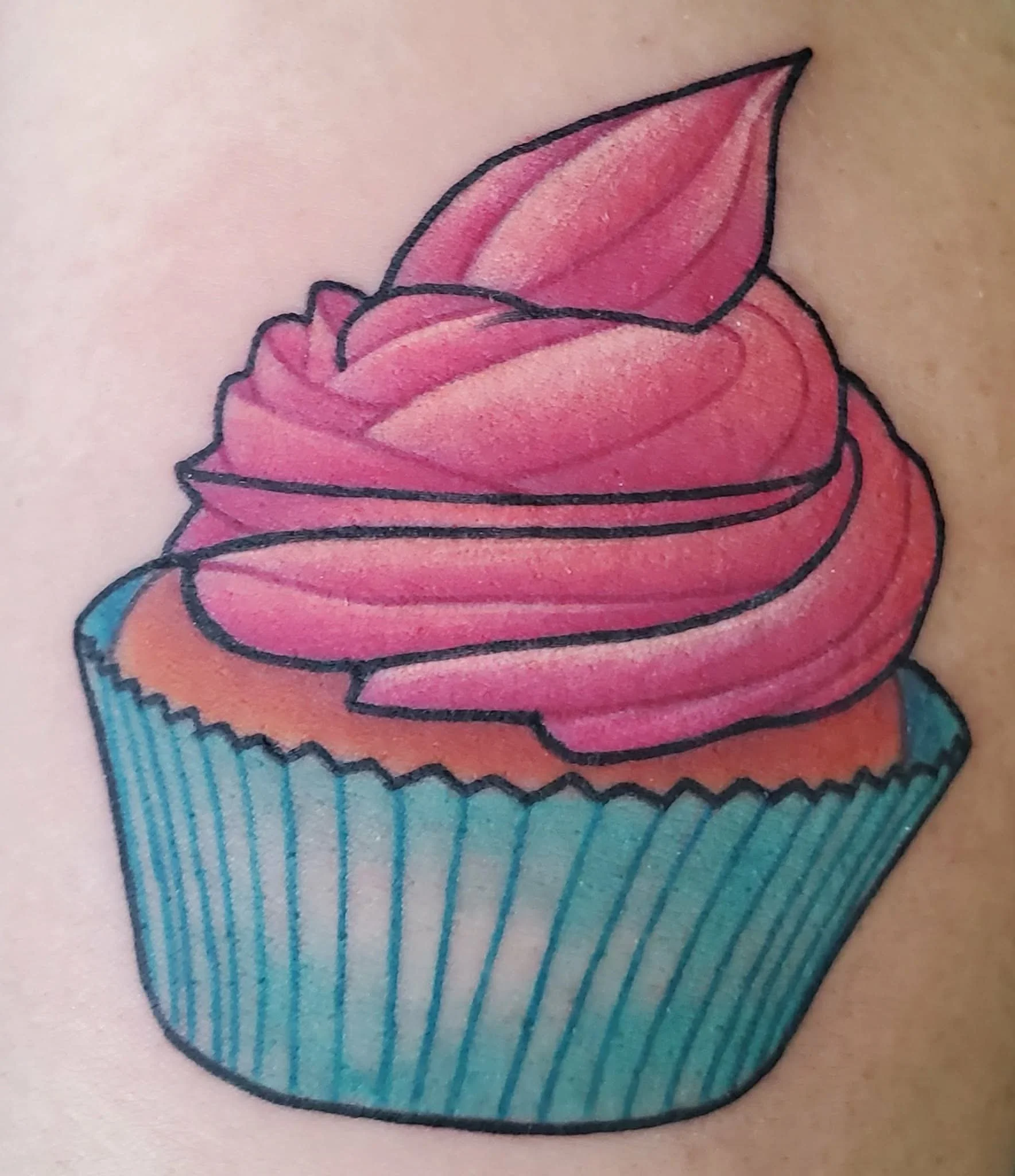 Colorful cupcake tattoo with pink frosting and a blue striped cupcake liner.