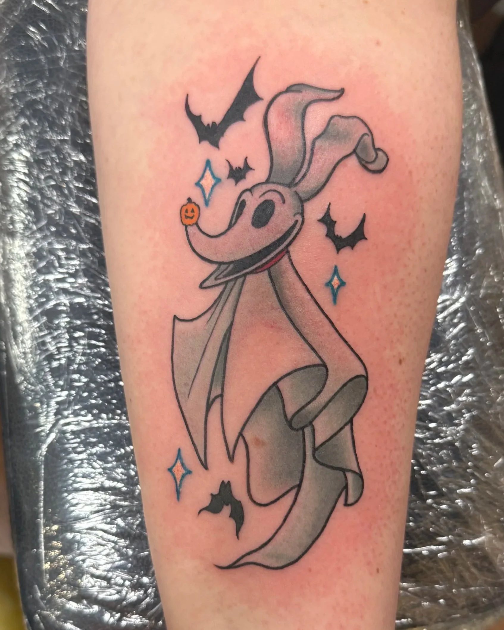 A tattoo of Nightmare Before Christmas character Zero surrounded by small bats and sparkles.