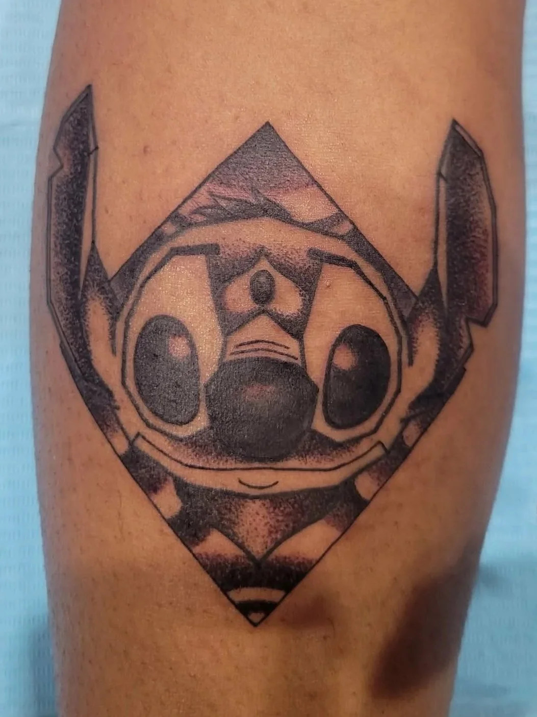 Tattoo of Stitch from Lilo & Stitch on a person's arm, in black ink with shaded details.
