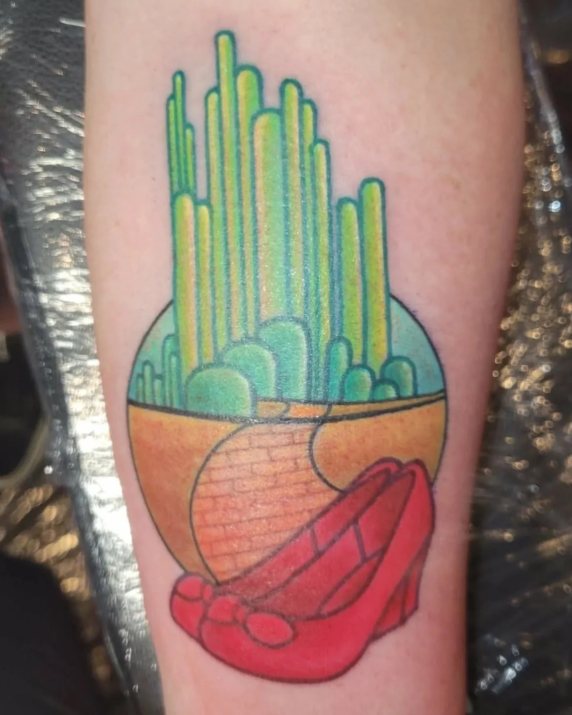 Colorful tattoo of Wizard of Oz Emerald City, the yellow brick road, and red ruby slippers.