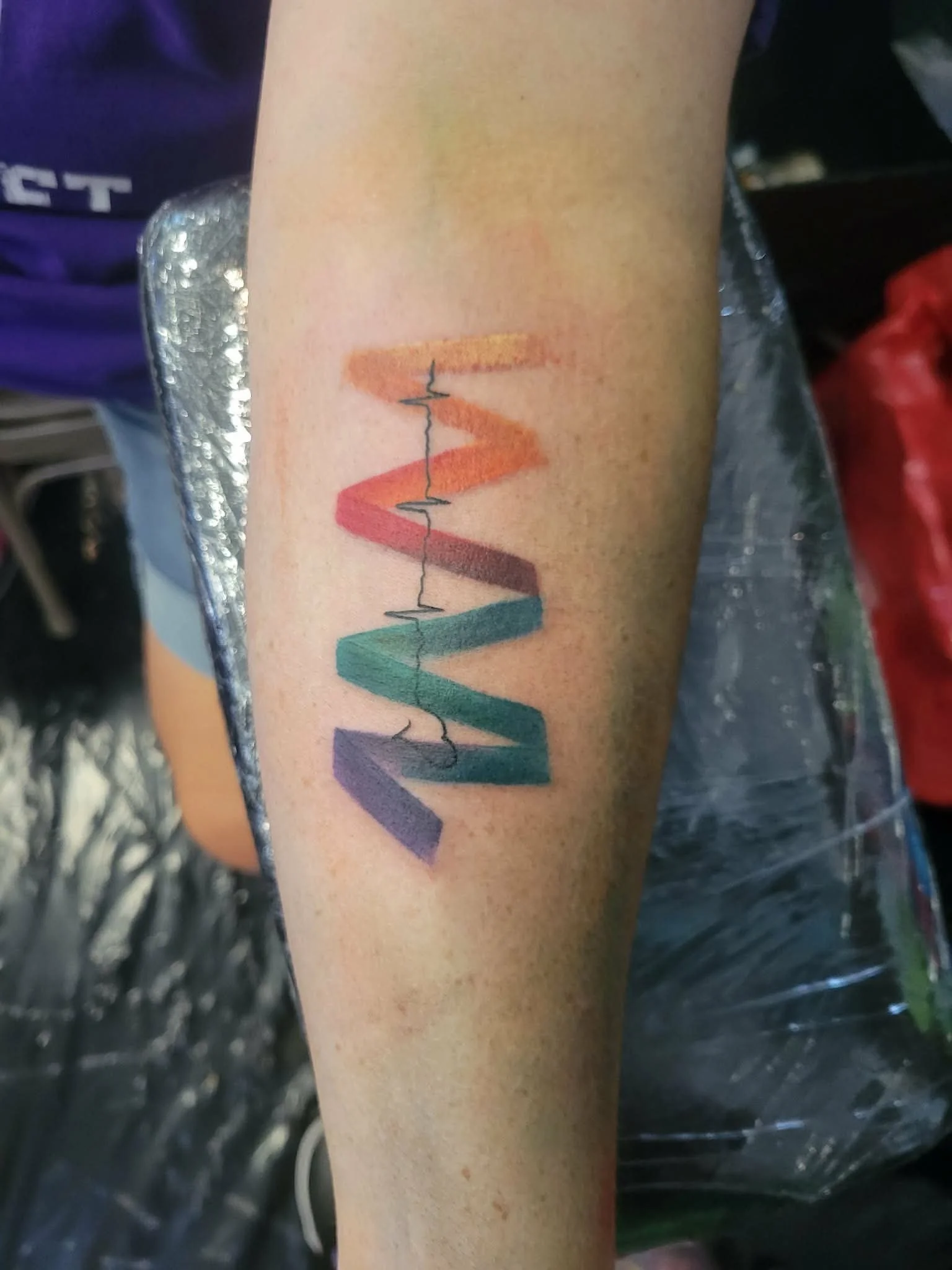 Tattoo of the word 'LOVE' in rainbow colors on a person's forearm.